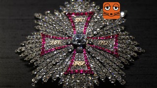 Ein sternförmiger Orden mit weißen und pinken Diamanten, die ein Kreuz darstellen, liegt vor einem schwarzen Hintergrund.